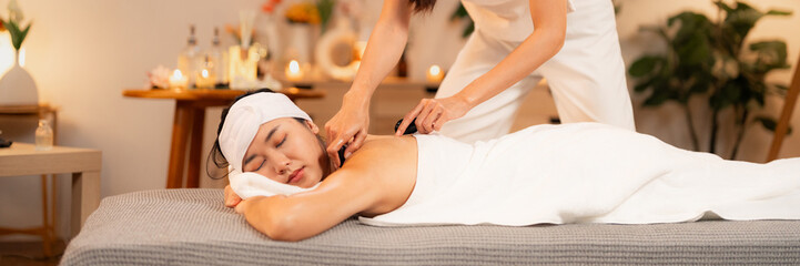 Asian woman receives relaxing hot stone massage therapy at luxurious spa center for ultimate wellness and stress relief provided by professional therapist