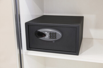 Black electronic safe with a digital keypad installed on a white shelf, concept of security,...