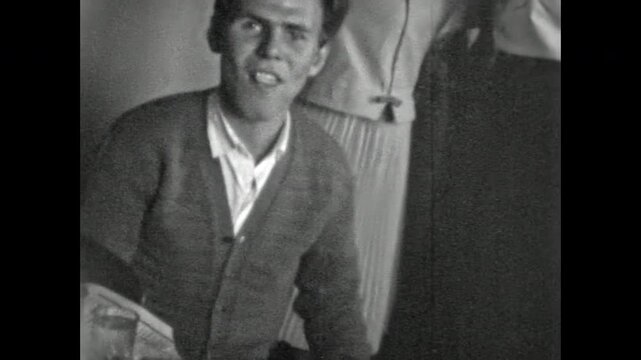 Cheerful man laughs, eating cake at lively gathering. Friends dance, celebrate around him, capturing a joyful, carefree moment of happiness. Old film. Archival retro 1960s. Vintage archive.