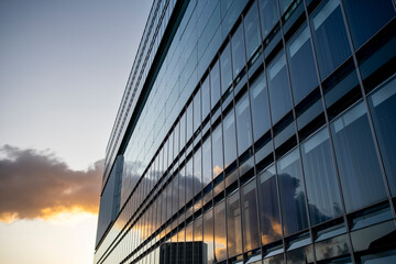 Low angle view of modern corporate glass tower reflecting warm sunset sky expressing transparency, growth, and economic optimism within contemporary urban architecture