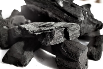 Fototapeta premium Black natural lump charcoal pieces piled on a white background: Illustrates natural grilling fuel, raw energy, purifying elements, and bold texture for design
