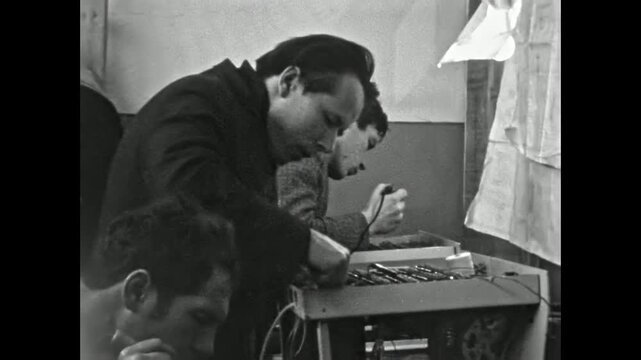 Electronics technicians solder microchips at production. Workers solder microcircuit focusing on assembly, board repair. Industrial manufacturing at factory. Old film. Archival retro. Vintage archive