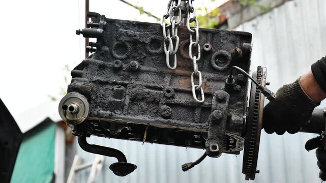Mechanic repairing old engine block with chains and tool