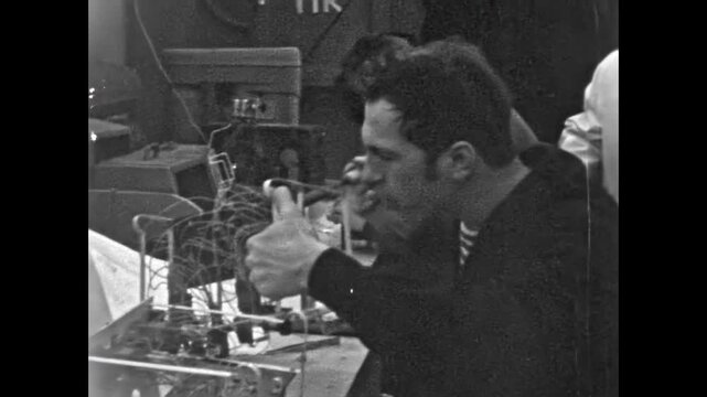 Technician man solders components on electronic circuit board technology at factory equipment. Manufacturing, engineering in industrial production. Old film. Archival retro 1960s. Vintage archive