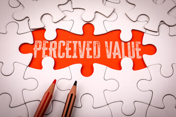 Phrase perceived value written on red background under white puzzle pieces symbolizing marketing psychology pricing and customer perception concept