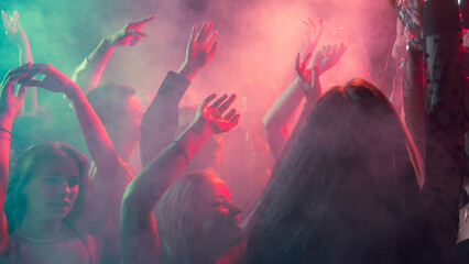 Christmas crowd raising hands through red and turquoise light haze. Concept of festive event branding, emotional connection, youth culture, and nightlife visuals