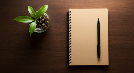 Overhead view of a tan spiral notebook with black pen and green plant in glass jar image