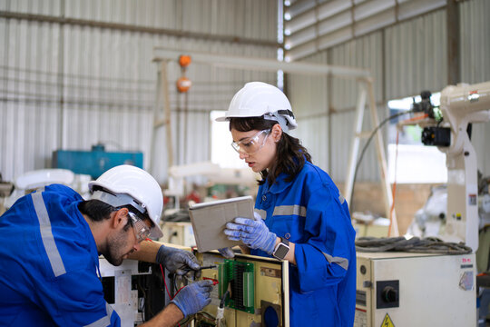Blue collar workers at machine shop with welding robot arm.