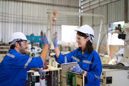 Blue collar workers at machine shop with welding robot arm.