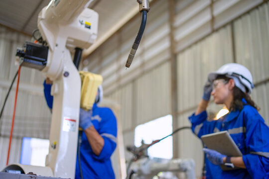 Blue collar workers at machine shop with welding robot arm.