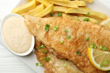 British Traditional Fish and chips with sauce, lemon and green onion on white wooden table, top view
