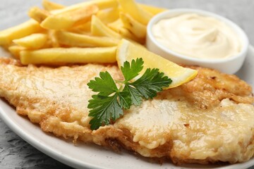 British Traditional Fish and chips with sauce, lemon and parsley on table, closeup