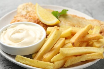 British Traditional Fish and chips with sauce, lemon and parsley on gray table, closeup