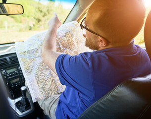 Man tourist sits in passenger's seat of car, holding large map, pointing towards windshield....
