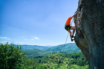 Aerial view of male rock climber ascending rugged limestone cliff with harness and rope for safety....