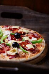 Pizza with chorizo ​​sausage, mozzarella cheese, green pepper and black olives. Rustic wooden background. Soft focus.	