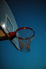 A basketball hoop at night, illuminated by artificial lights, creating a dramatic atmosphere. A basketball hoop and net illuminated by harsh, dramatic artificial lights at night. Strong shadows are