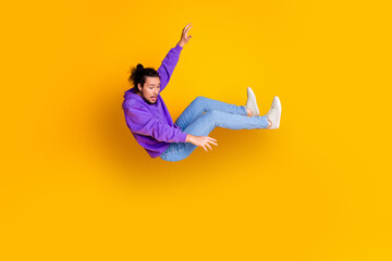 Young man in casual purple hoodie falling against vibrant yellow background, expressing surprise and joy in a dynamic pose