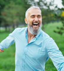 Happy active mid aged adult couple having fun walking running holding hands and bonding in park or...