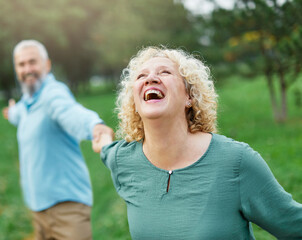 Happy active mid aged adult couple having fun walking running holding hands and bonding in park or...