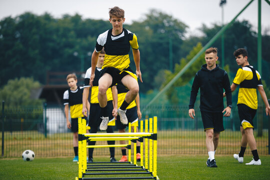 Player kick soccer ball to coach and ladder skipping. Teenagers on soccer training camp. Boys practice football with young coaches. Junior level athletes improving soccer skills on outdoor training - Powered by Adobe