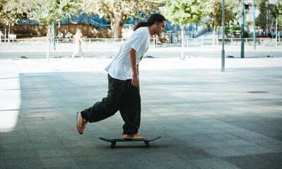 Fototapeta premium Young skater cruising through the city on a sunny afternoon