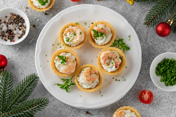 Christmas food. Tartlets with shrimp, cream cheese, garlic and parsley on a wooden board on gray concrete background.
