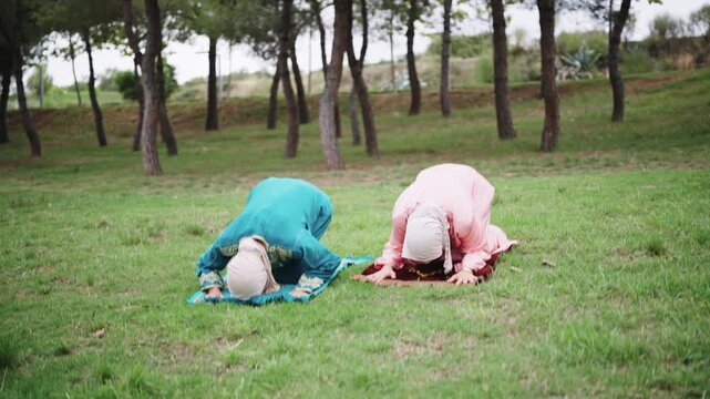 Muslim women in hijabs praying outdoors on mats