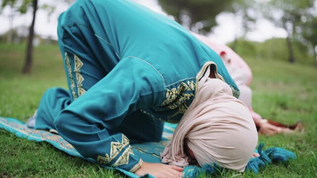 Muslim women in hijab praying namaz outdoors on green grass