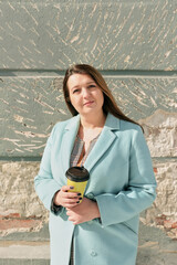 Portrait of woman standing outdoors holding takeaway coffee cup looking into camera with relaxed...