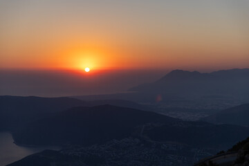 A tranquil sunset slides below distant mountains, casting warm orange light