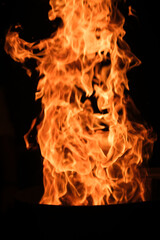 Fototapeta premium A dramatic, close-up shot of a towering, intense column of fire, with vivid orange and yellow flames rising against a dark, black background.