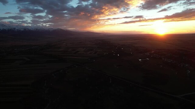 Majestic Sunset Over Expansive Landscape with Mountains in the Background and Glowing Horizon Illuminating the Sky, Captured from an Aerial Perspective