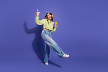 Young woman in casual style dancing joyfully while listening to music on headphones with a...