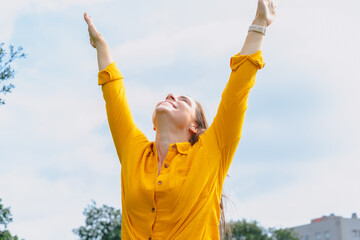 Joyful young woman outdoors raising arms to the sky celebrating freedom and success. Positive...