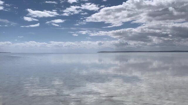 Normal shot video of a salt lake with slightly rippling water caused by gentle wind, under a partly cloudy sky