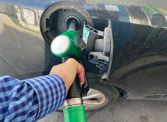 Manguera de surtidor de gasolina para llenar depósito en la mano echando combustible en el tanque...