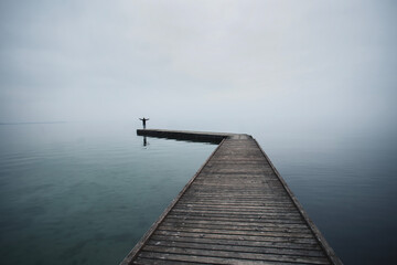 Obraz premium Man with arms raised against the light at the end of a pier on the sea in the evening light