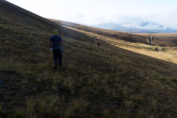 Obraz premium A group of hikers ascending a sunlit mountain slope in the early morning light. The warm tones of sunrise highlight endurance, teamwork, and exploration in nature.