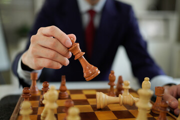 Person suit holding wood chess king piece above chessboard with other yellow chess pieces focus,...