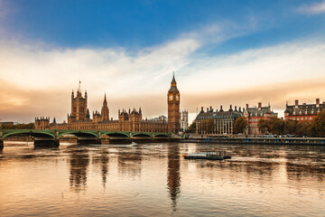 Fototapeta premium Palace of Westminster and Elizabeth Tower reflecting in River Thames under blue and golden sky in London