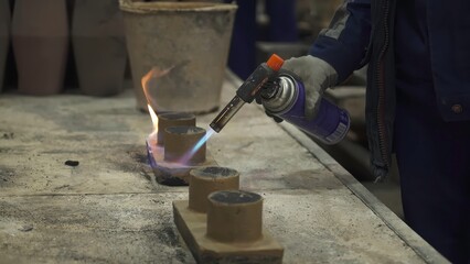 Foundry worker using blowtorch on small clay cylinders. Stock clip