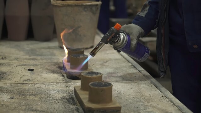 Foundry worker using blowtorch on small clay cylinders. Stock clip