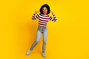 Fototapeta premium Funny young woman in casual striped top posing against vibrant yellow backdrop with a joyful peace hand gesture