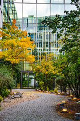 Obraz premium Modern Office Building With Autumn Garden Pathway: Contemporary Glass Architecture Surrounded By Colorful Trees And Soft Evening Lights In Urban Setting