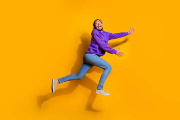 Energetic young man jumping joyfully in purple hoodie and jeans against bright yellow background showcasing fun style