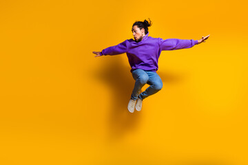 Obraz premium Dynamic young man wearing vibrant purple hoodie jumping in midair on a yellow background, expressing energy and fun
