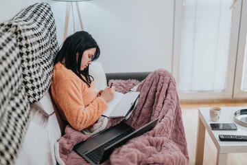 A young woman writing in a notebook while relaxing on a sofa in comfort