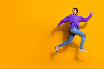Happy young man in a vibrant purple hoodie leaping energetically against a bright yellow backdrop conveying joy and excitement