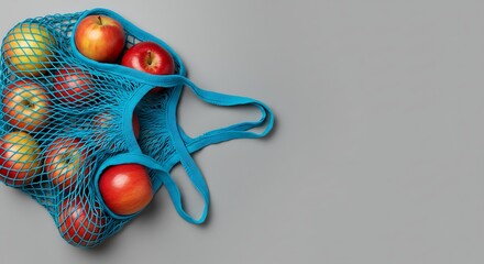 Fresh apples in reusable mesh bag against gray background with copy space